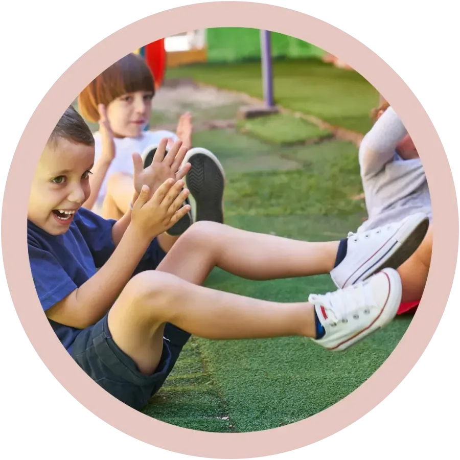Kinder sitzen draussen auf dem Rasen und klatschen im Rhythmus in die Hände, spielerische Lern- und Wahrnehmungsförderung